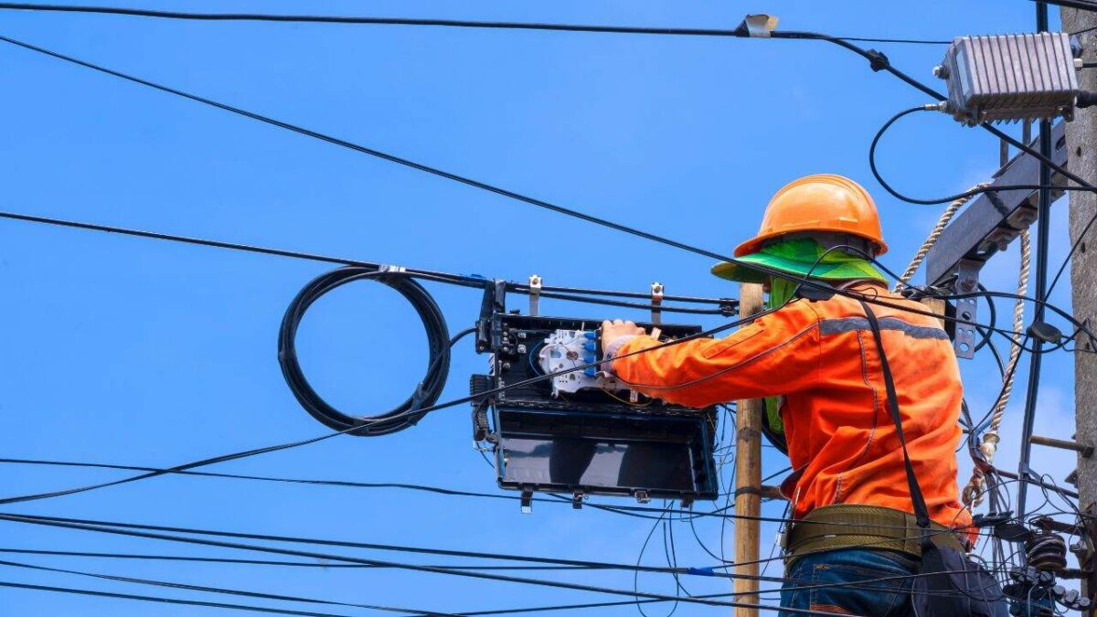 Vue arrière du technicien sur une échelle en bois travaille à l'installation de la fibre optique et du répartiteur sur le poteau électrique sur fond de ciel bleu