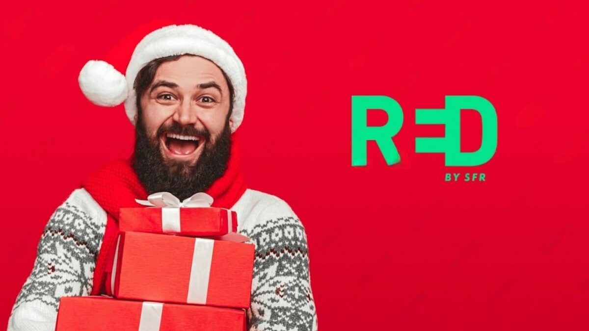 Un homme heureux avec un bonnet de père de noël, et se tenant à côté du logo de Red by SFR