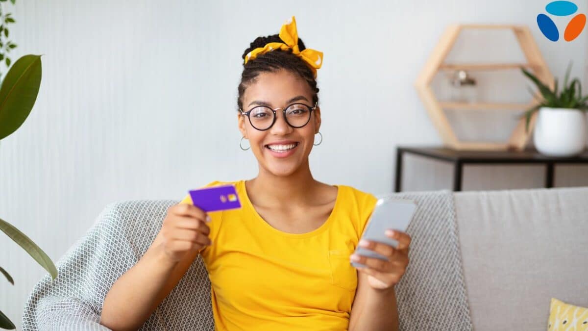 Concept d'achat en ligne. Femme noire heureuse à lunettes tenant et utilisant un smartphone et une carte de crédit